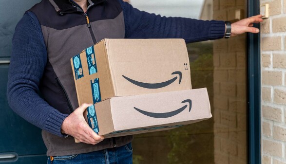 Ein Paketbote klingelt mit mehreren Amazon-Paketen an einer Haustür.