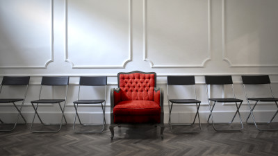 Ein roter, üppiger Sessel inmitten einer Reihe karger Stühle © ﻿﻿olly, Adobe Stock