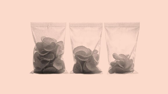 Drei durchsichtige Chipst&uuml;ten in abnehmender F&uuml;llmenge von links nach rechts: Die linke T&uuml;te ist fast vollst&auml;ndig mit Chips gef&uuml;llt, die mittlere etwa zur H&auml;lfte, die rechte nur noch zu einem Viertel, wodurch die zunehmende Shrinkflation visualisiert wird.