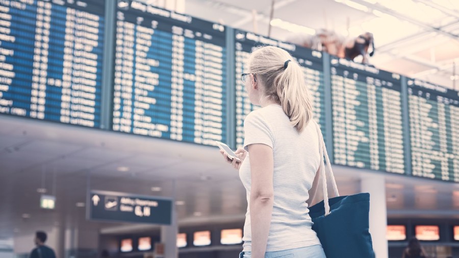 Frau blickt auf Abflugtafel am Flughafen © Sergey Furtaev, Adobe Stock
