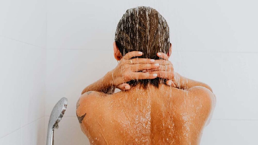 Eine Frau steht mit dem Rücken zur Kamera unter einer Dusche.
