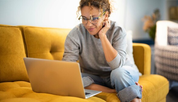 Eine Frau sitzt auf einer Couch am Laptop.