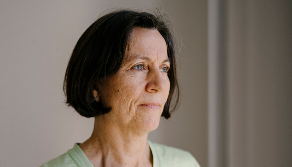 Portr&auml;tfoto von Maria Lackner, Krankenschwester. Eine Frau mittleren Alters mit kurzem, dunklem Haar und blauen Augen blickt nachdenklich zur Seite. Sie tr&auml;gt ein hellgr&uuml;nes T-Shirt. Der Hintergrund ist schlicht und hell gehalten.