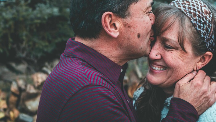 Ein älterer Mann küsst seine lachende Frau auf die Stirn