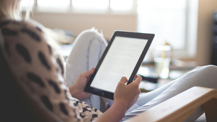 Eine Frau sitzt auf einem Stuhl und hält ein Tablet in der Hand.