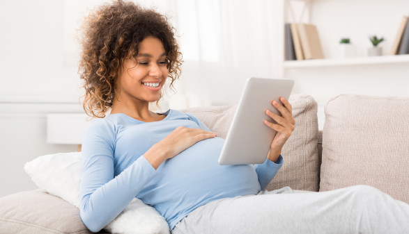 Schwangere mit Tablet am Sofa